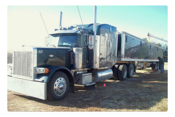 A black Peterbilt semi-truck attached to a black grain trailer being loaded