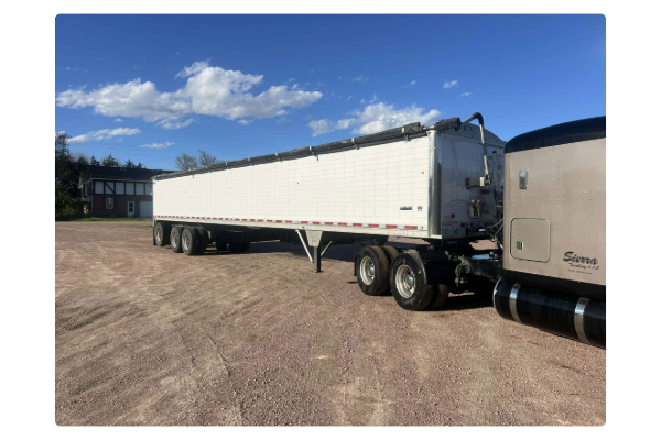 A shiny white belt trailer connected to a brown semi-truck with 